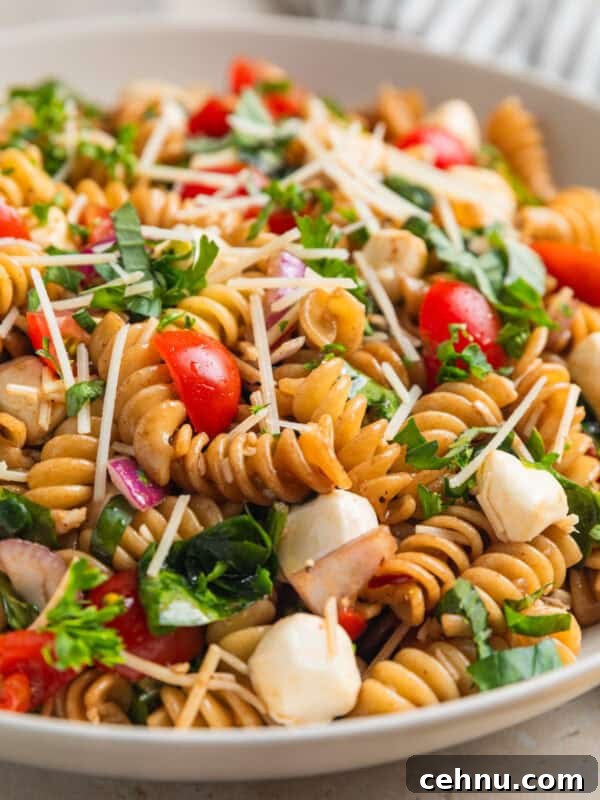 Pasta salad made with grape tomatoes, spinach, basil, mozzarella and other ingredients in serving bowl.
