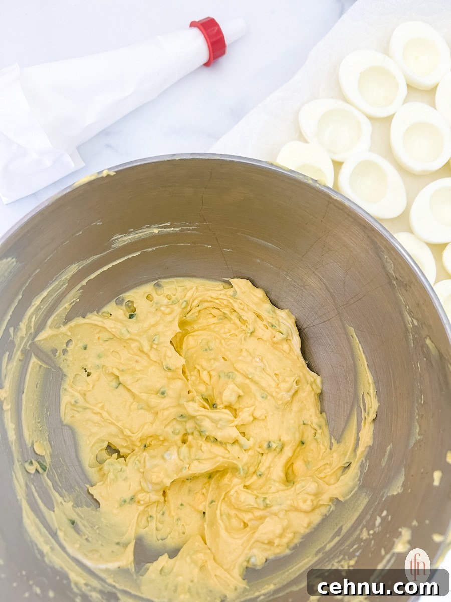 Egg yolk mixture on a stainless mixing bowl with piping bag and sliced boiled eggs without egg yolks.