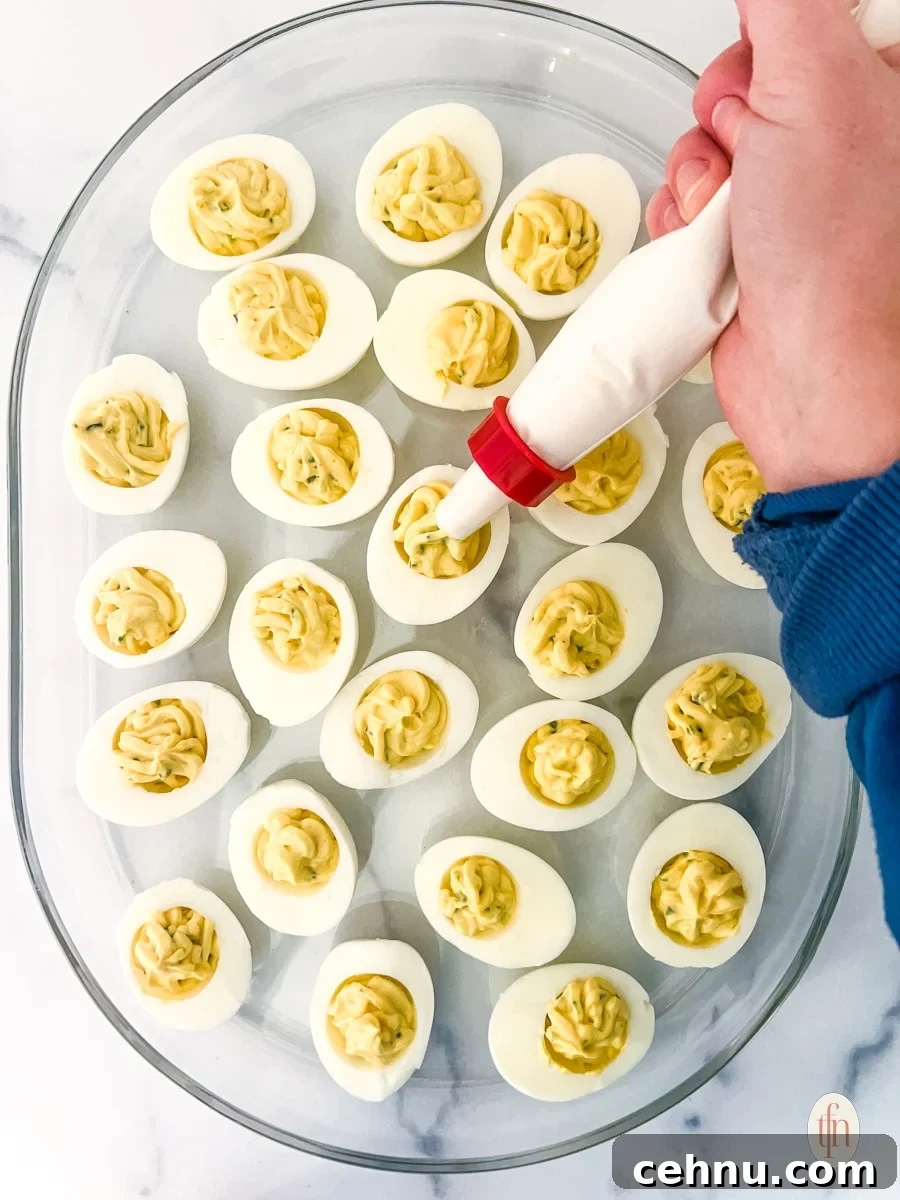 Egg yolk mixture being piped onto the sliced boiled eggs to make deviled eggs with bacon and jalapeno.