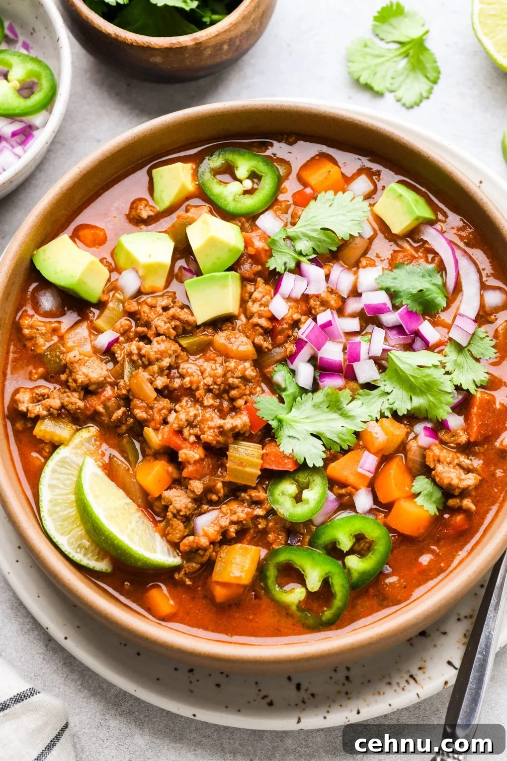 Colorful bowl of beanless Whole30 chili topped with avocado, red onion, cilantro, sliced jalapeno, and lime wedges.