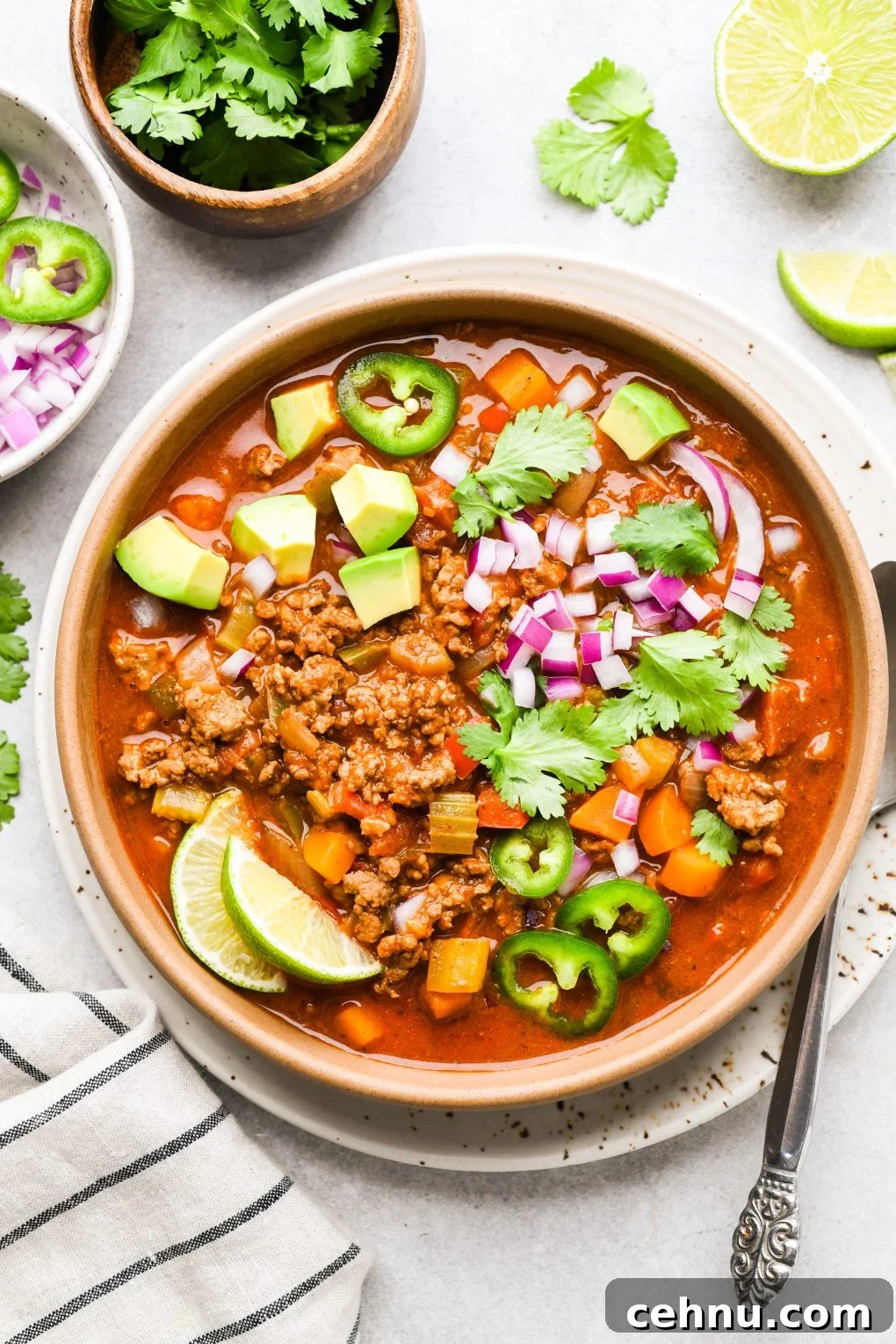 Colorful bowl of beanless Whole30 chili topped with avocado, red onion, cilantro, sliced jalapeno, and lime wedges.