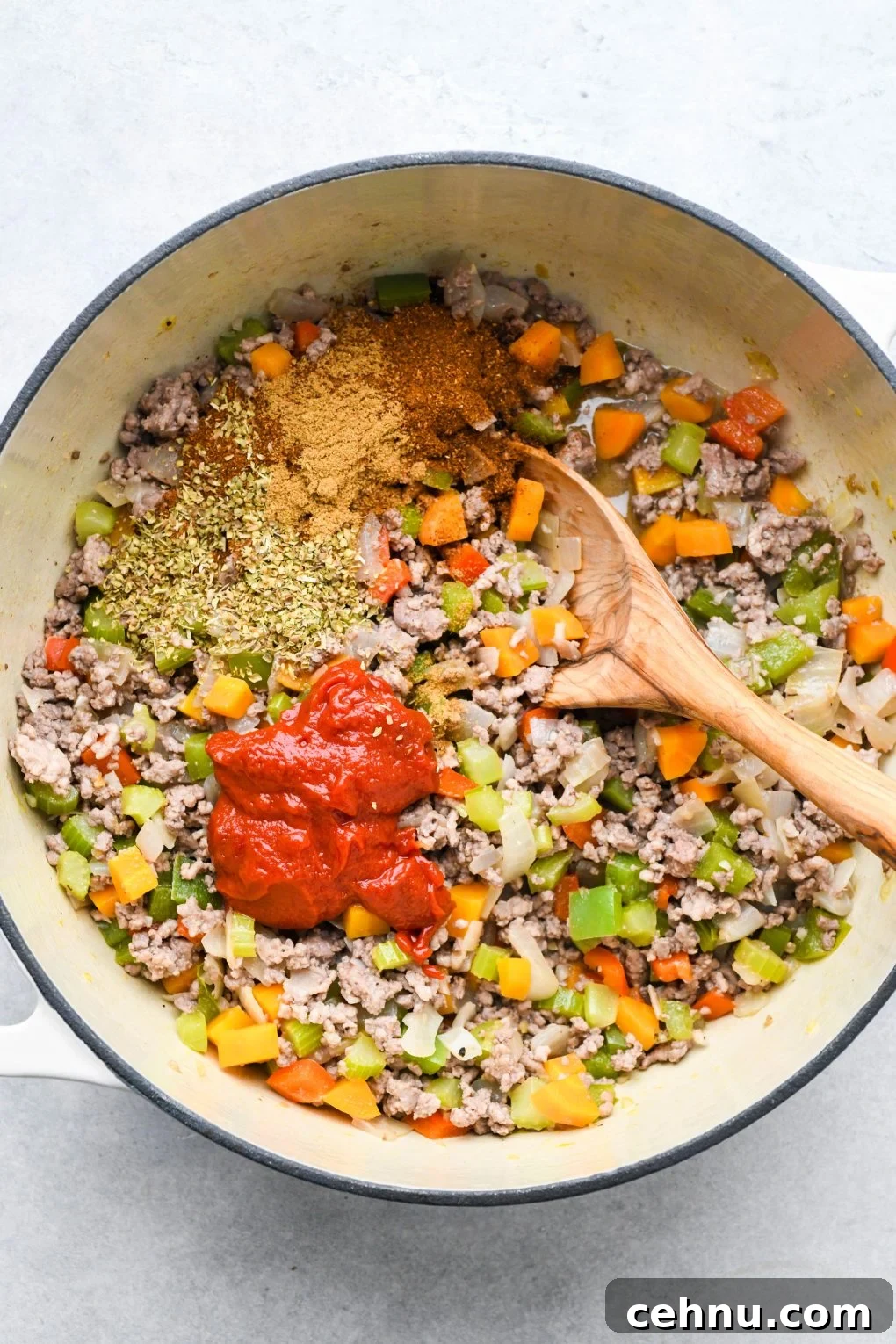 Veggies and meat with spices and tomato paste cooked in a large soup pot.