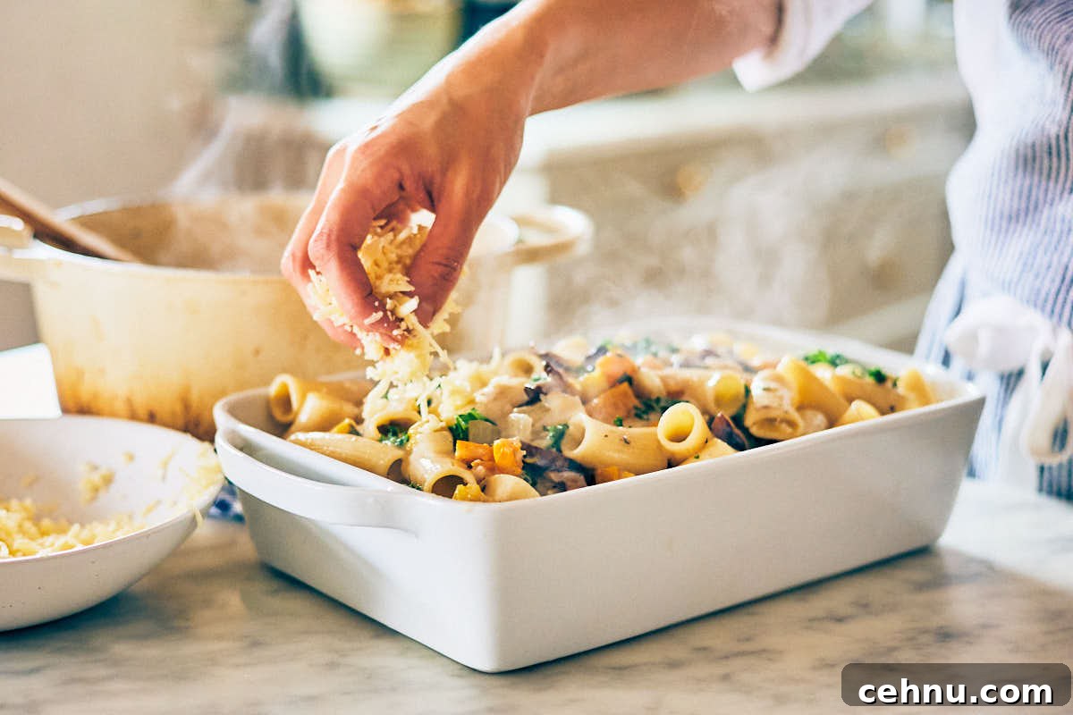 Butternut squash pasta being topped with cheese in a casserole dish.