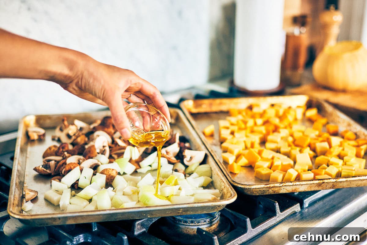 Oil drizzling over butternut squash, mushrooms, and onion on baking sheets.