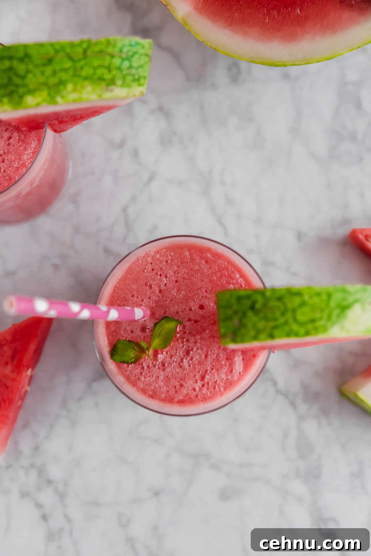 Frozen Watermelon Rose Wine Slushies 3 An aerial view of a glass with frozen watermelon rosé wine slushie with a watermelon wedge and pink straw and watermelon slices on a marble table.