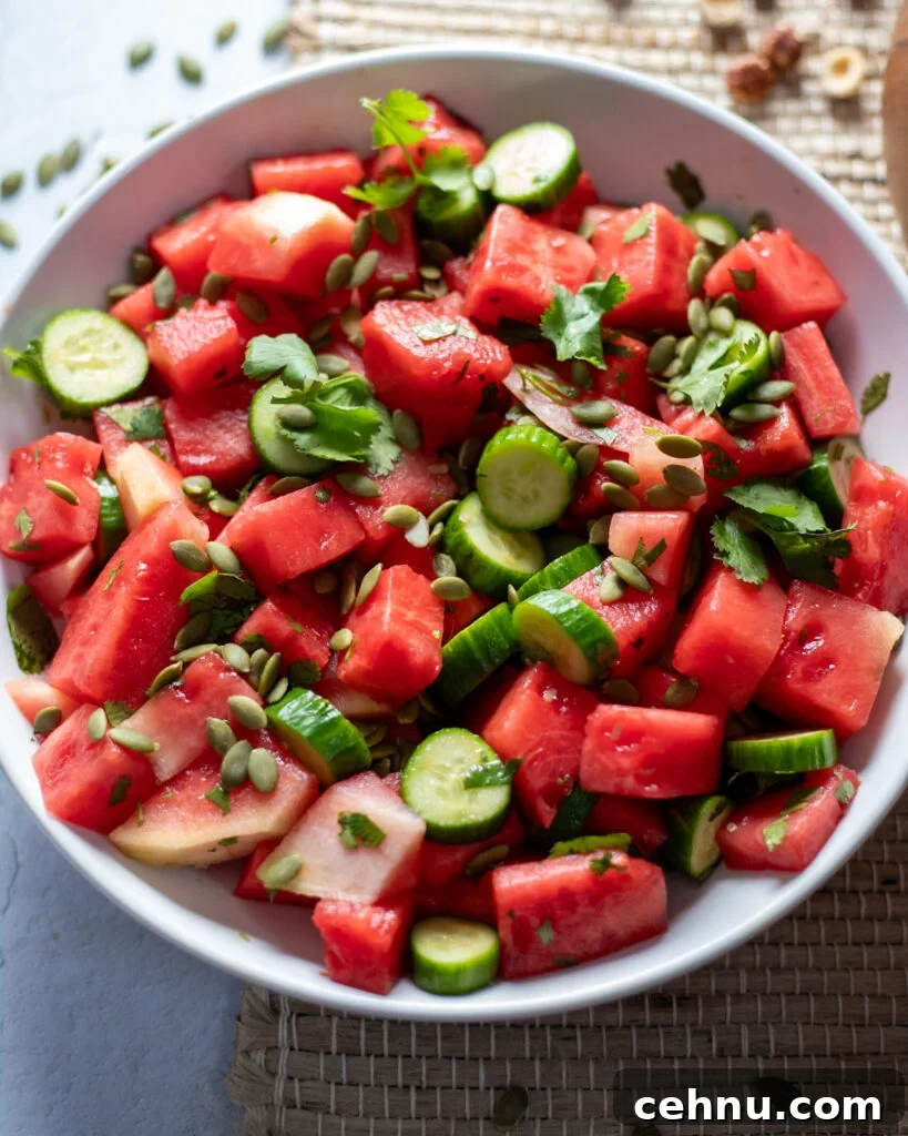 Light blue ceramic bowl filled with chopped watermelon, cucumbers, pepitas and cilantro with a white balsamic vinegar dressing