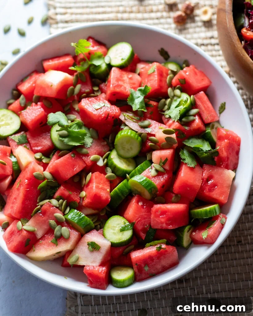 light blue bowl of a hydrating cucumber watermelon salad made with watermelon, cucumbers, cilantro and pepitas covered with tangy white balsamic vinegar salad dressing