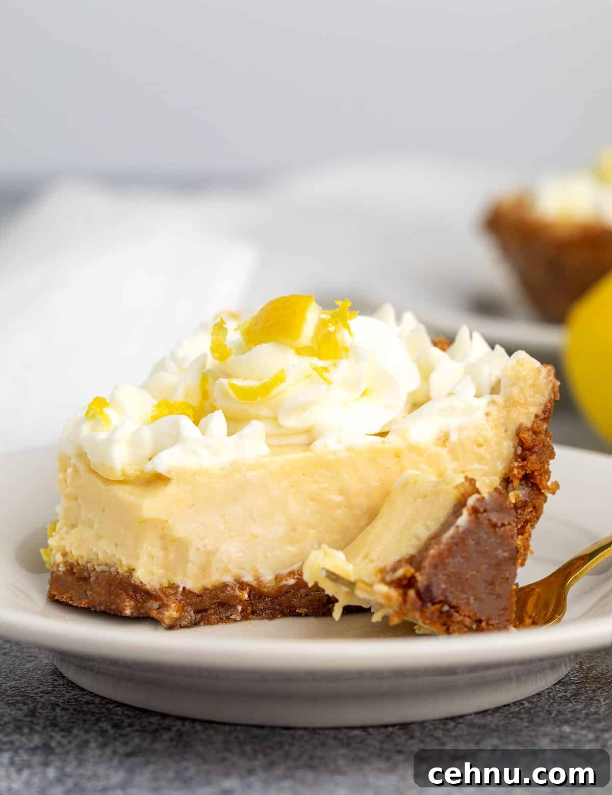 Slice of lemon pie with a cookie crust and whipped cream on a white plate, a forkful taken out to show the smooth texture