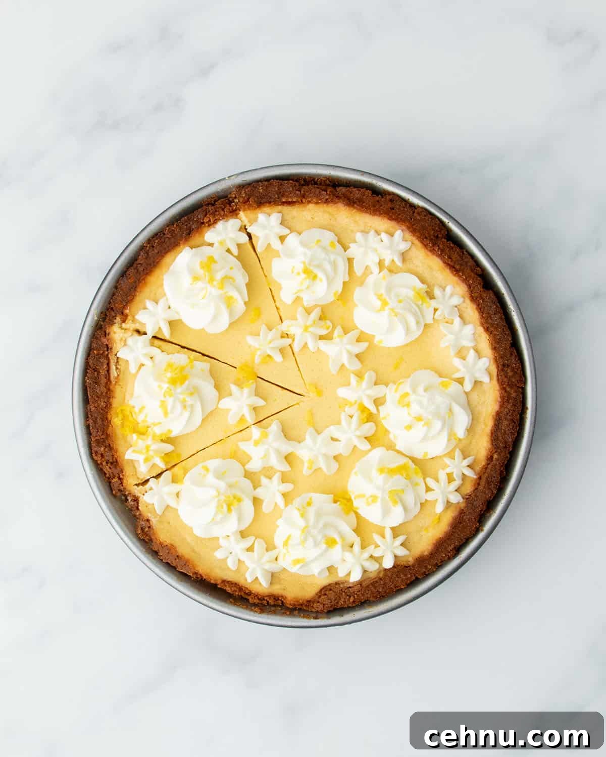 Fully baked lemon pie decorated with piped whipped cream and lemon zest, with a few slices cut but not removed.