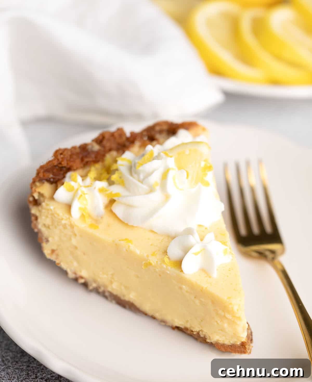 Slice of chilled lemon pie topped with whipped cream and lemon zest, served with a gold fork