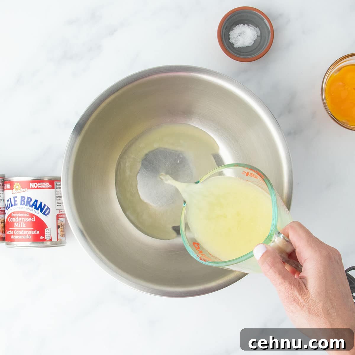 Lemon juice being poured into a large mixing bowl, surrounded by other ingredients on a marble surface.