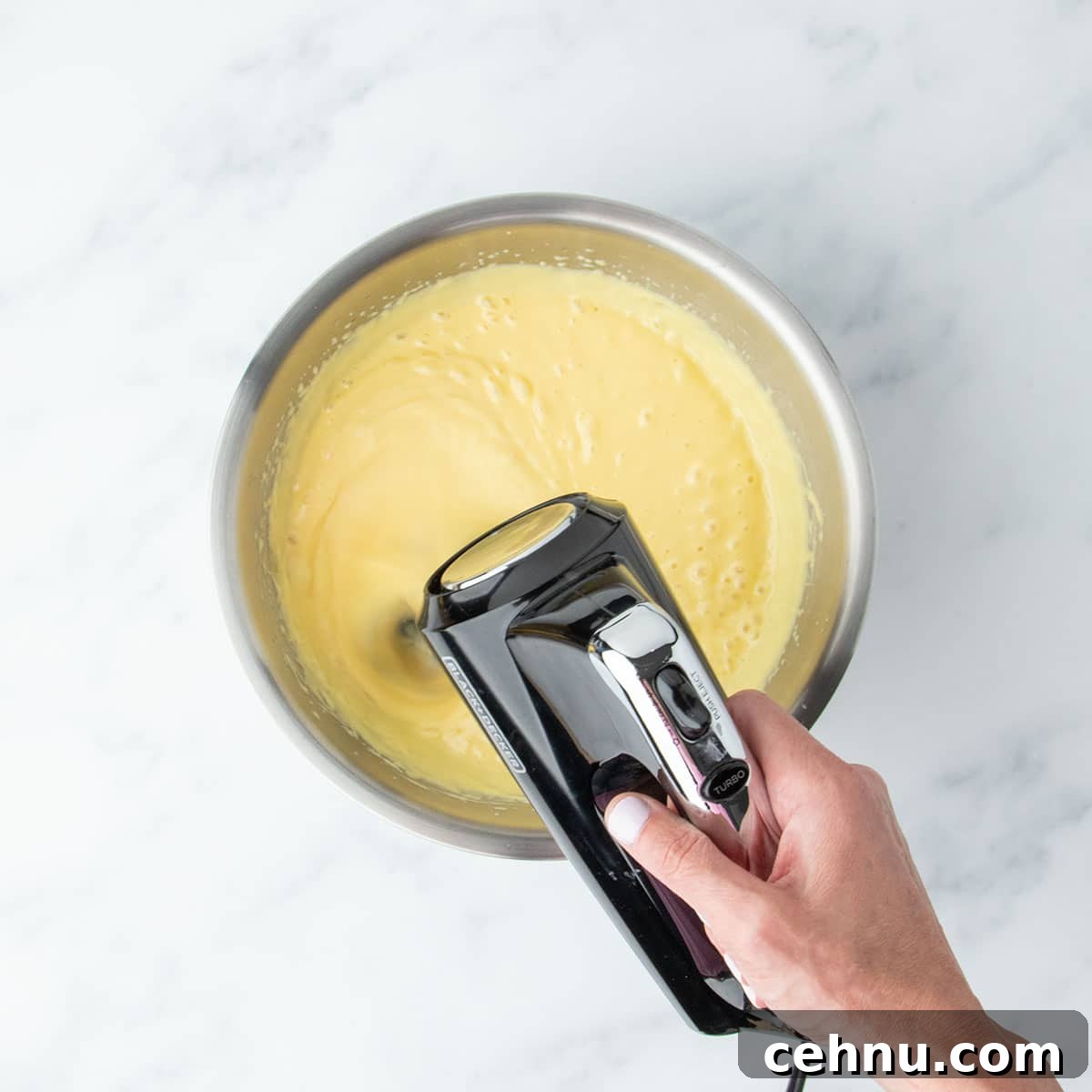 Hand mixer whipping the lemon pie filling in a metal bowl until smooth and creamy.