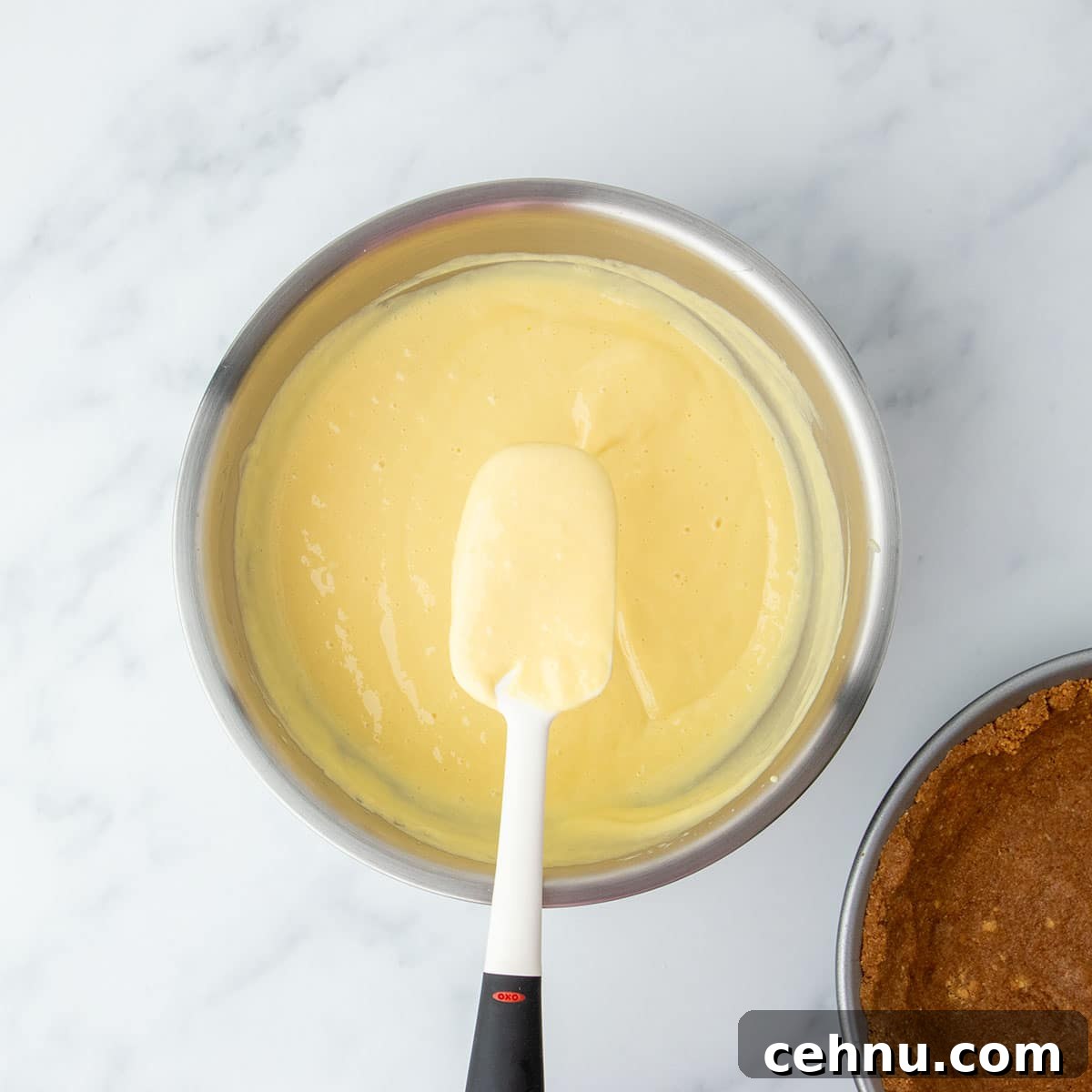 Spatula resting in a bowl of smooth lemon filling, ready to be poured into the crust.