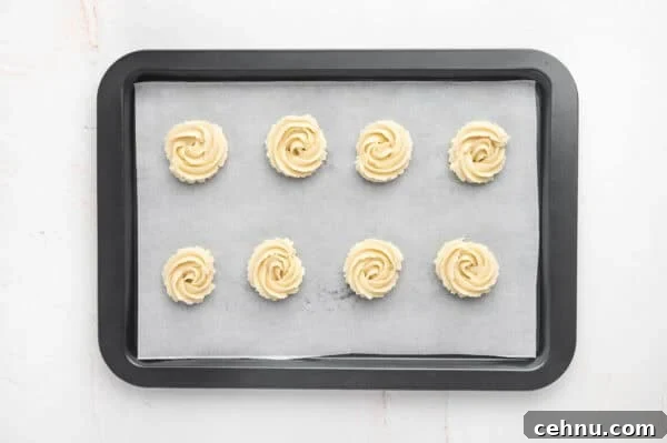 Classic Butter Cookies Recipe for Tea Time 10 Swirls of butter cookie dough on a parchment lined baking sheet.