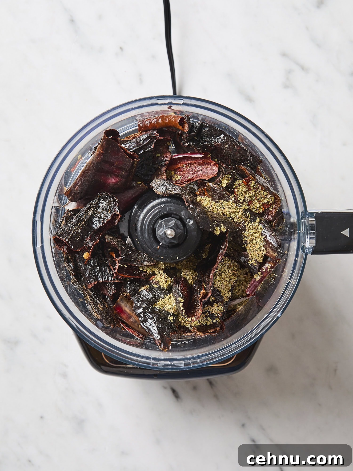 Food processor with cut up dried chiles before being ground up.