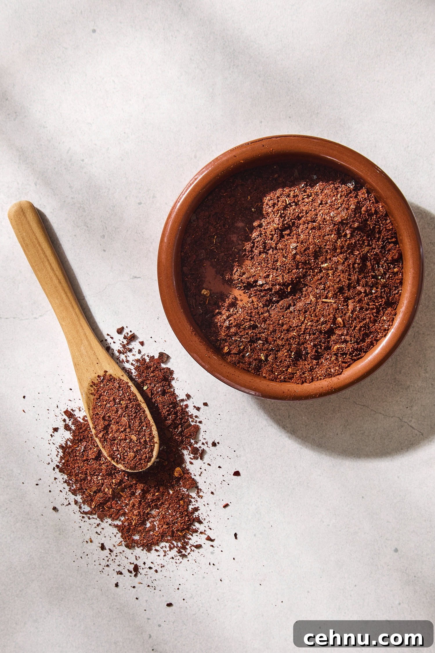 Brown bowl filled with homemade chili powder with a spoon scooping some.
