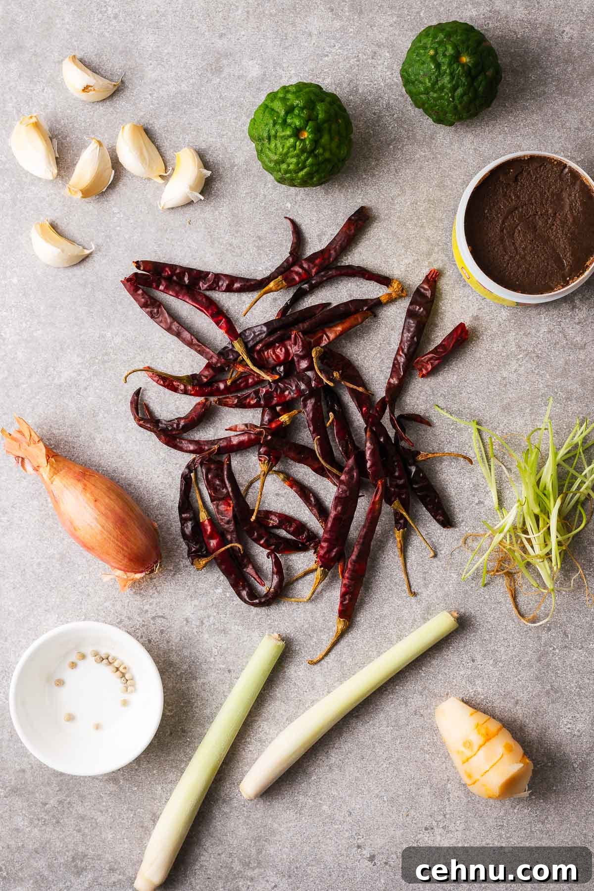 Thai red curry paste ingredients including shallot, kaffir limes, cilantro roots, lemongrass stalks, galangal, kaffir limes, shrimp paste, whole garlic cloves and white peppercorns.