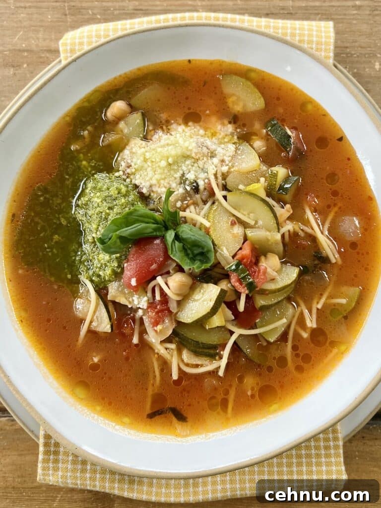 Italian zucchini soup in white bowl with basil pesto, grated cheese and basil sprig garnish.