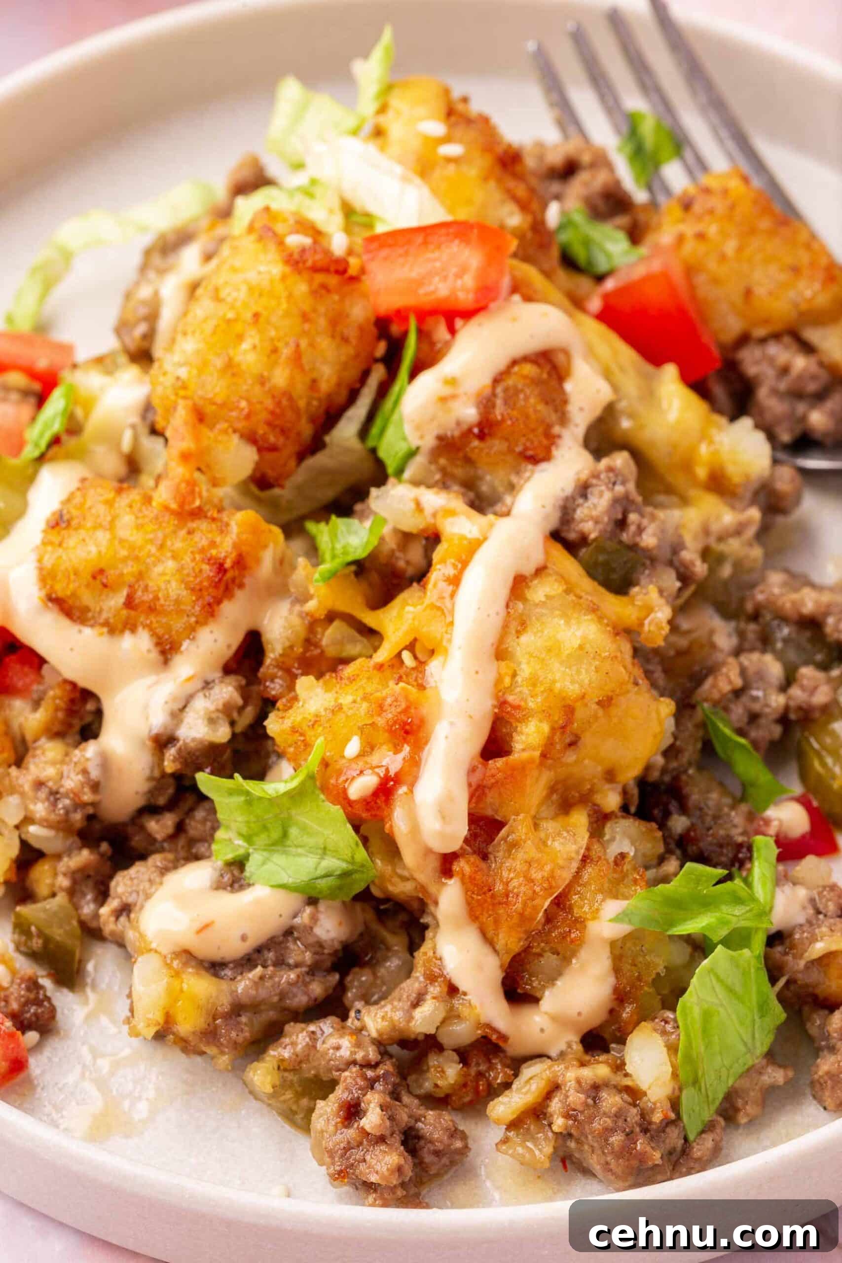 A close up of a single serving of big mac casserole with tater tots and ground beef on a salad plate with a fork.