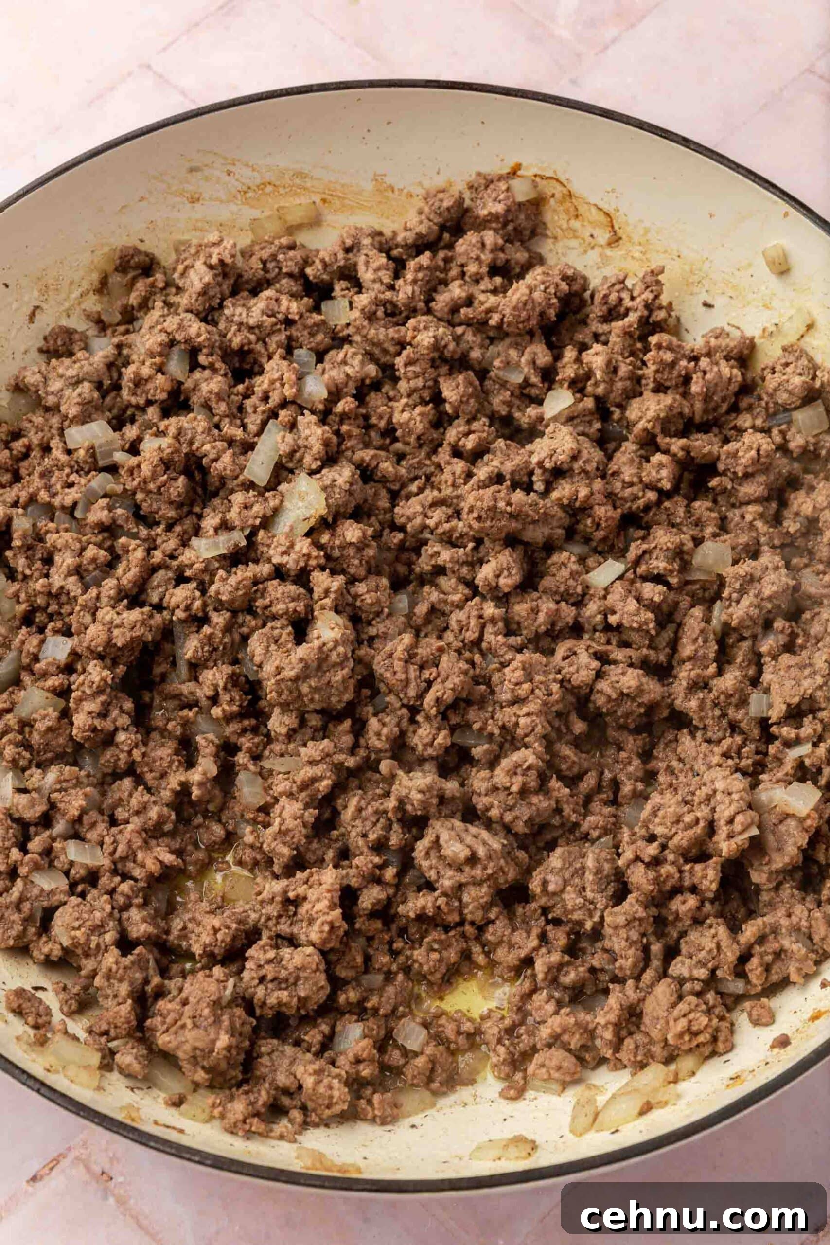 Cooked ground beef and diced onions in a round braising pan.