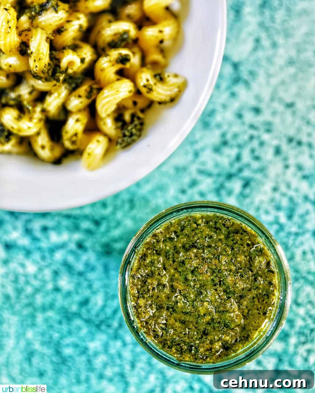 jar of mint pesto in the bottom right corner with bowl of pesto pasta in the top left corner, all on a bright blue background.