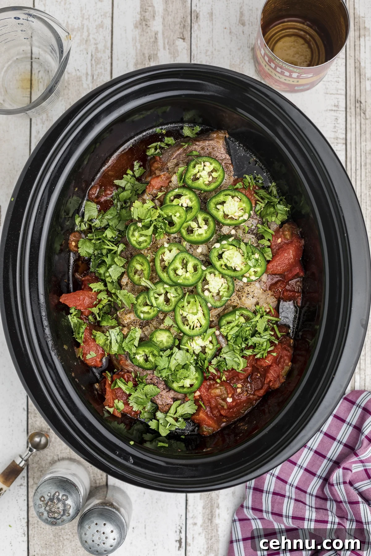 The chuck roast, tomatoes, jalapenos, and cilantro in a crockpot.