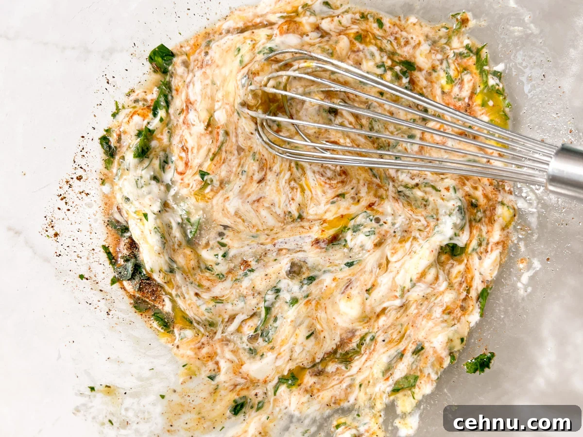 Crispy Gluten Free Crab Cakes Recipe with Lemon Dill Sauce 4 Whisk mixing creamy crab cake base with herbs and spices in a glass bowl.