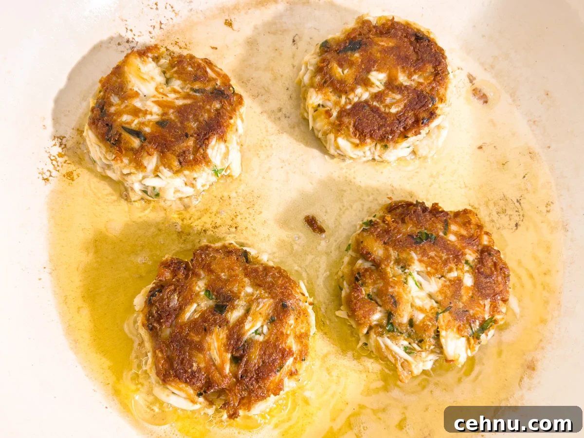 Crispy Gluten Free Crab Cakes Recipe with Lemon Dill Sauce 8 Gluten-free crab cakes frying in oil with golden brown crust forming.