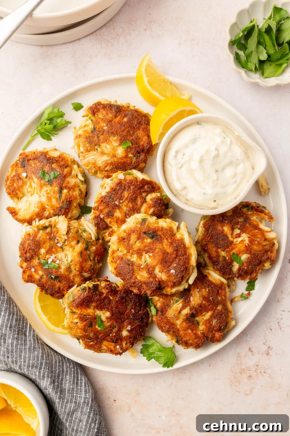 Crispy Gluten Free Crab Cakes Recipe with Lemon Dill Sauce 10 Full plate of gluten-free crab cakes arranged around a bowl of tartar sauce with lemon wedges and parsley