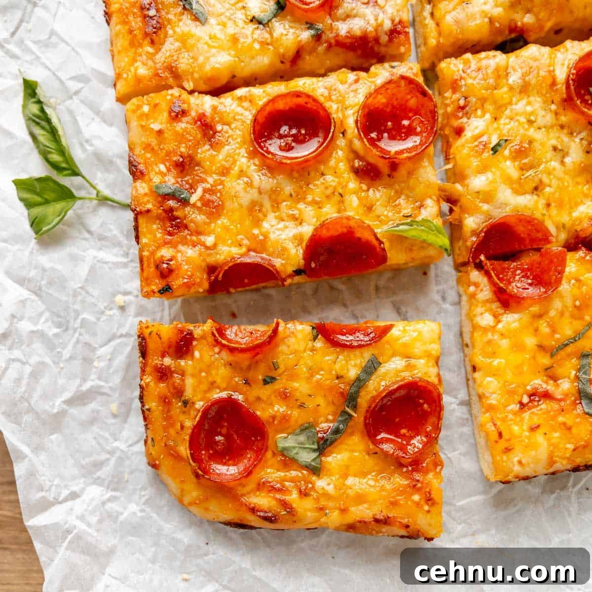 Rectangular slices of pepperoni pizza with melted cheese and basil leaves on parchment paper.