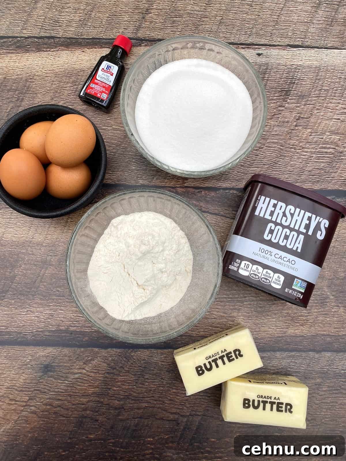 Homemade Brownie Mix Recipe for Fudgy Chocolate Brownies 3 Eggs, vanilla extract, flour, sugar, cocoa powder and two sticks of butter displayed on a plank.