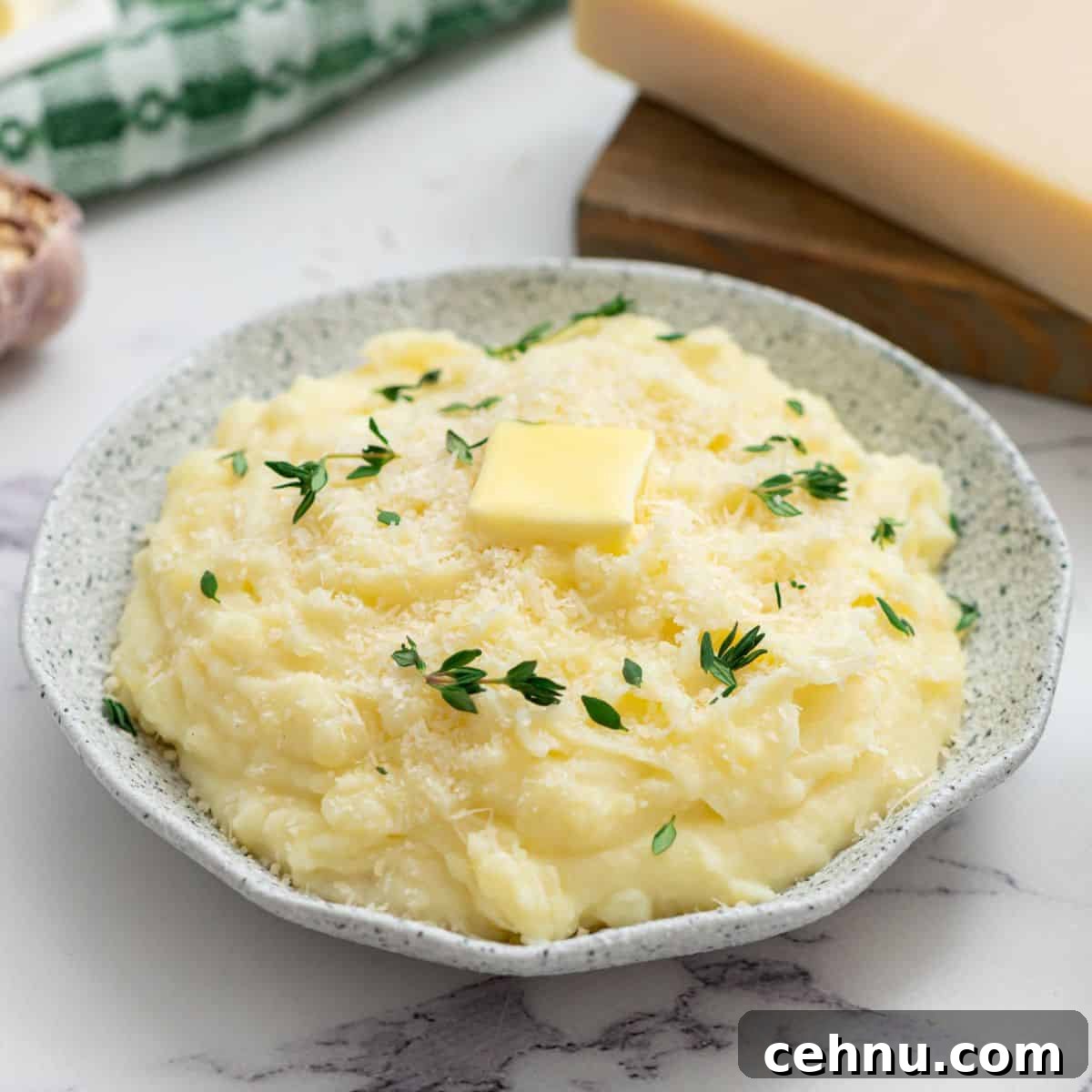 Crockpot mashed potatoes in serving bowl topped with parmesan, butter, and thyme.