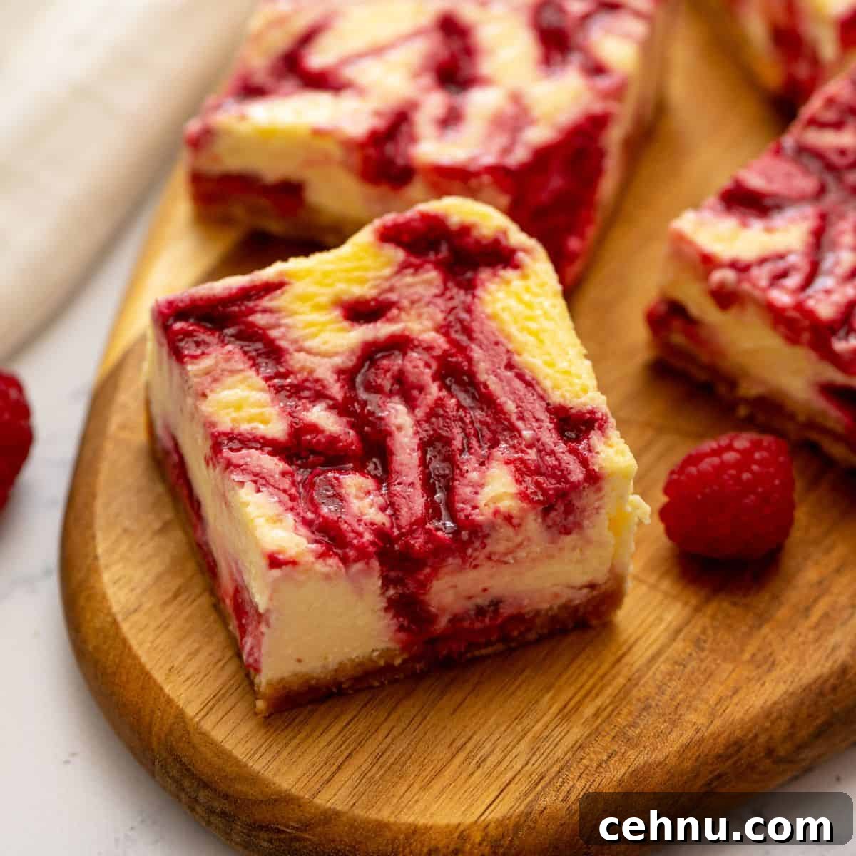 Sliced cheesecake bars on wooden cutting board revealing the raspberry swirl throughout the cheesecake batter.