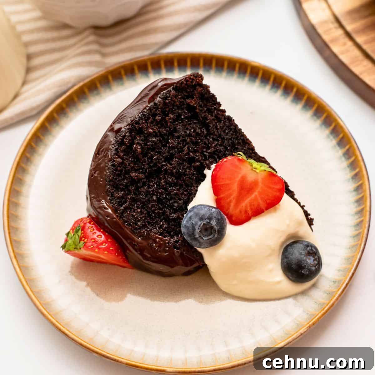 Slice of sour cream chocolate bundt cake iced with ganache topping on plate with berries and whipped cream.