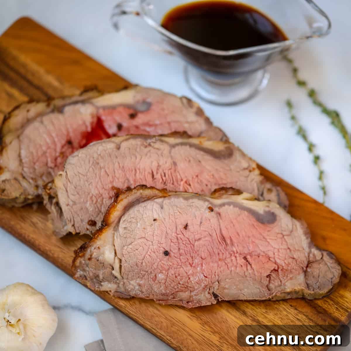 Sliced new york strip roast on cutting board with aus jus in background.