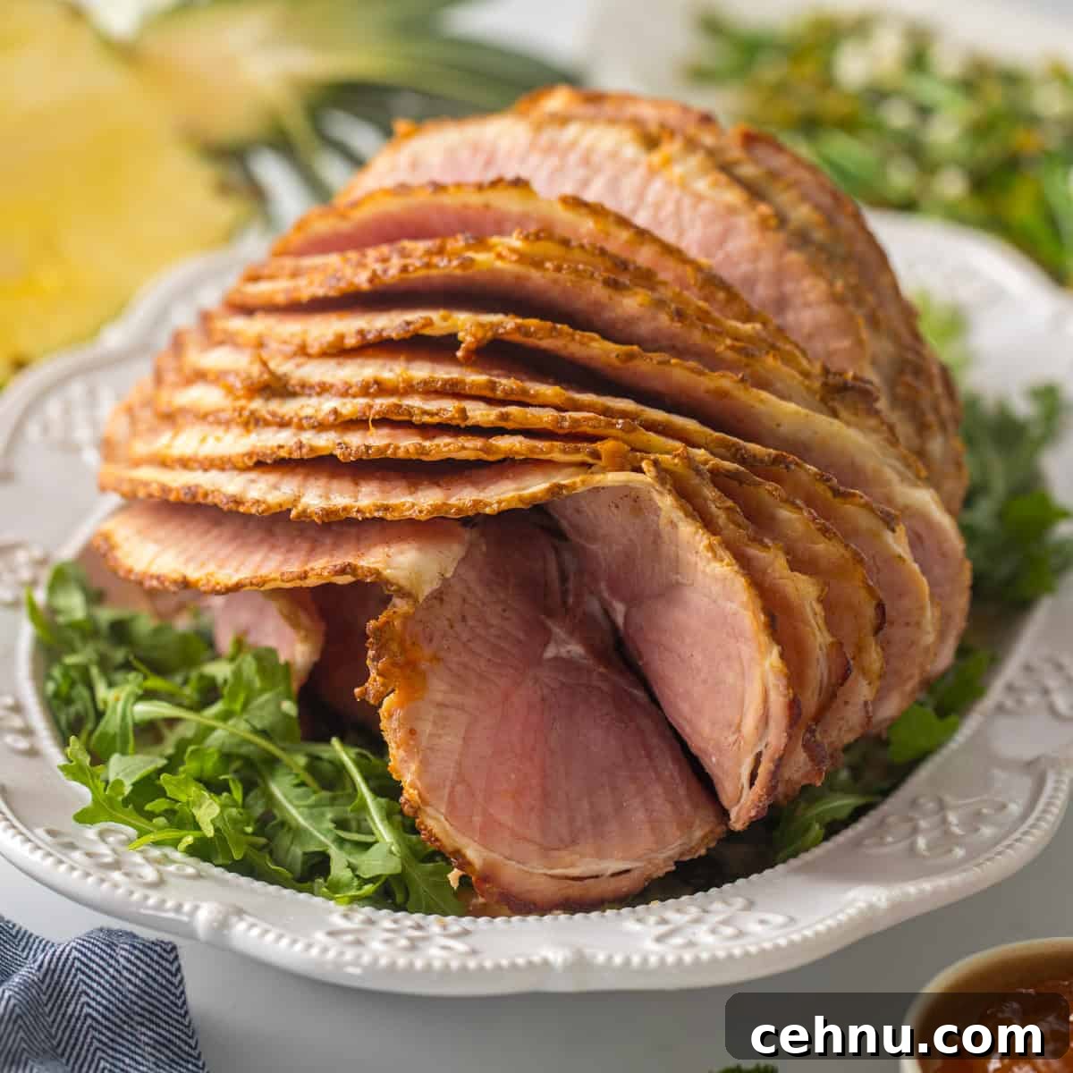 Spiral sliced ham on platter with pineapple glaze with fresh pineapple and asparagus salad in background.