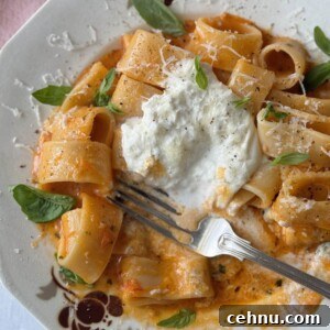 a white bowl with a fork filled with tomato butter pasta and topped with burrata.